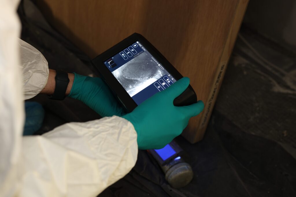 Photo of a person using a device to locate finger prints at a crime scene